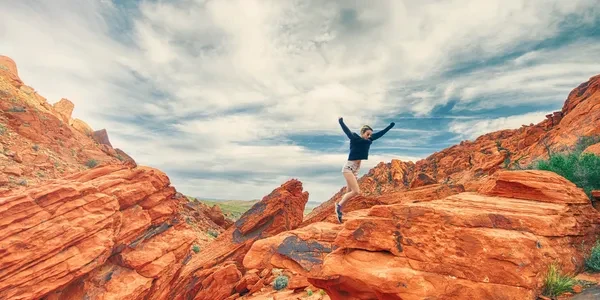 Person jumping triumphantly on red rock formations — symbol of resilience and freedom